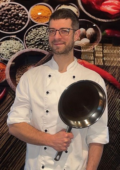 Robin Weiland Portrait mit einer Pfanne haltend im Weinhandel & Kochschule Robin in Schwerin