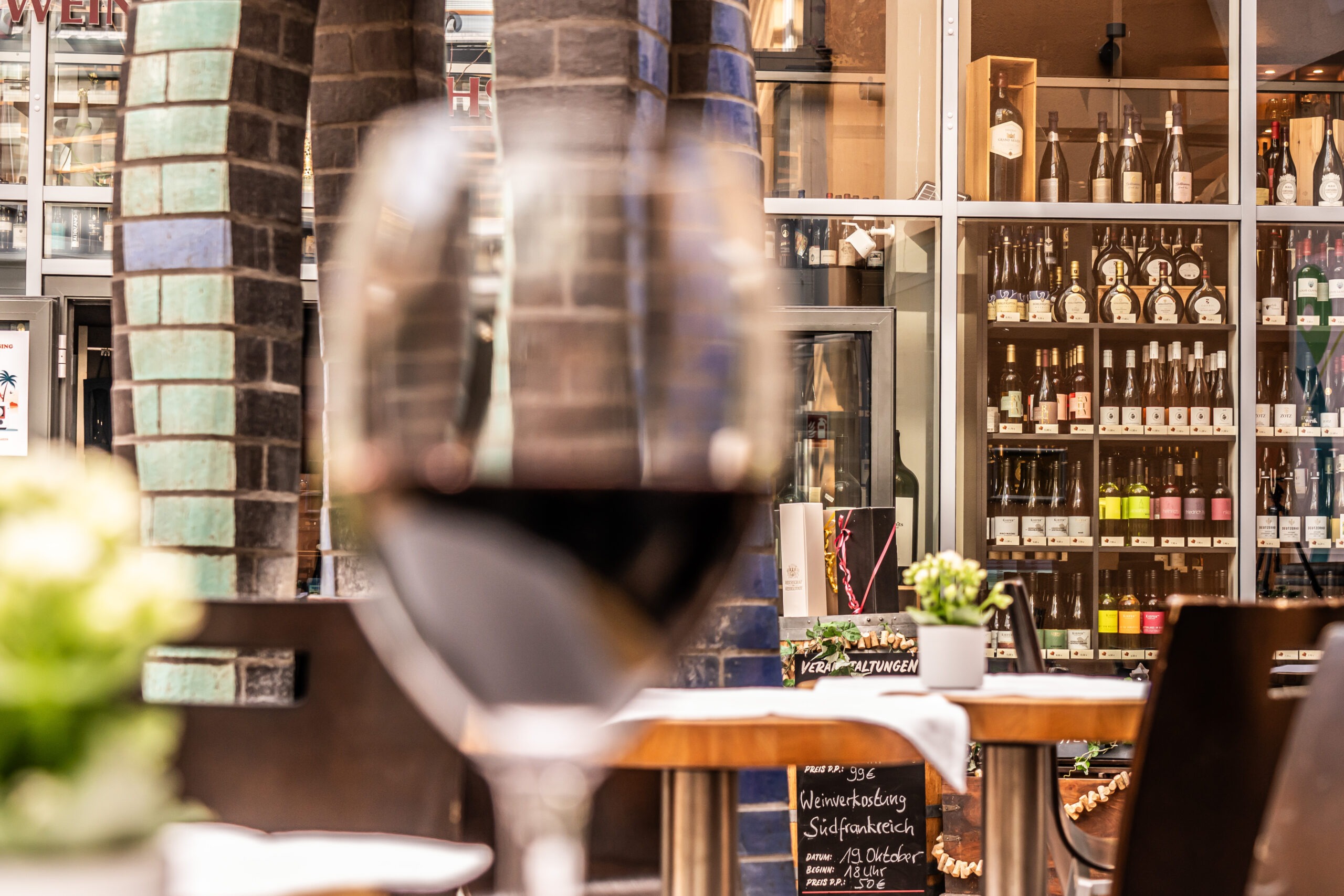 Foto eines Weinschrank im Hintergrund und unscharfen Rotwein-Glas im Vordergrund